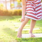 A child itching their leg with mosquitos swarming around them.