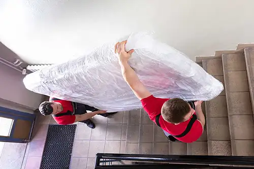 Movers hauling a plastic-covered mattress up stairs - Florida Pest Control, Gainesville FL